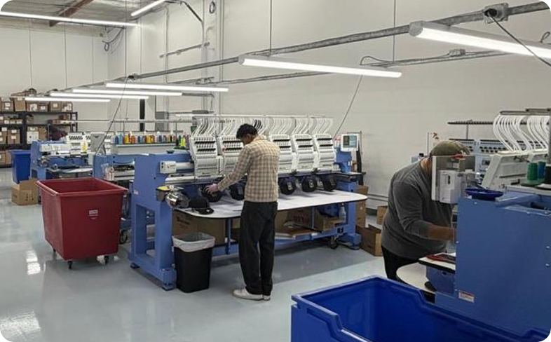 Production team operating embroidery machines in a custom apparel manufacturing and decoration facility.