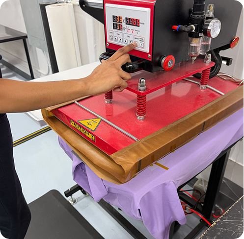 Heat press machine applying a custom design to a purple t-shirt in a professional apparel decoration shop.