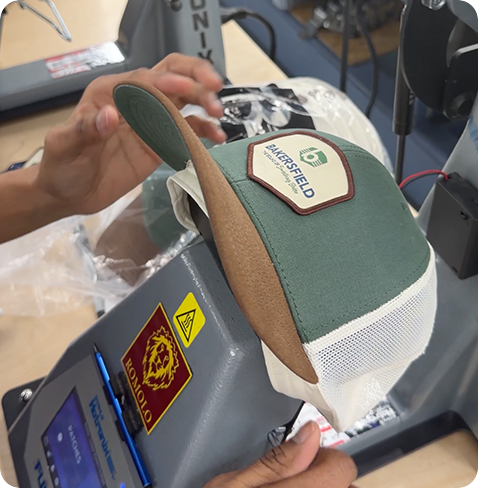 Applying a custom leather patch to a trucker cap using a professional heat press machine.